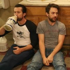 three men sitting on the floor drinking from bottles in front of a bathroom sink and toilet