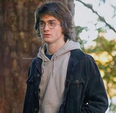 a young man wearing glasses standing next to a tree