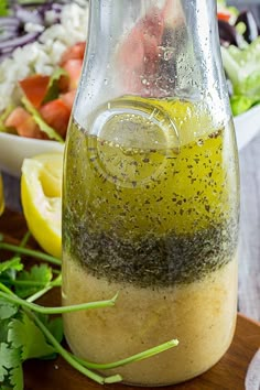 a bottle filled with dressing next to a bowl of salad and lemon wedges on a cutting board