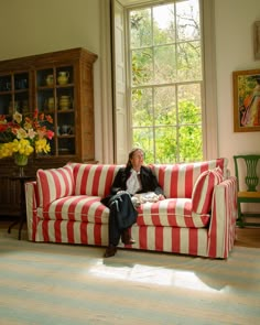 a woman sitting on top of a red and white striped couch next to a window