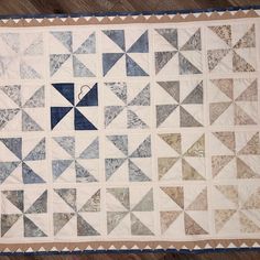 a quilted table topper with blue and white designs on it, sitting on a wooden floor