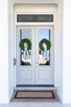 two wreaths on the front door of a house with blue ribbons hanging from them