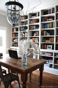 a laptop on a wooden table in front of a book shelf filled with lots of books