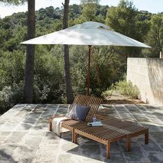 an umbrella and two lounge chairs on a stone patio with trees in the back ground