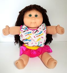 the doll is wearing a colorful shirt and pink skirt with her arms spread wide open