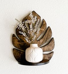 a white vase with some flowers in it on a shelf next to a wall decoration