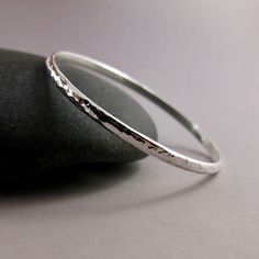 This stylish sterling silver bangle is handcrafted with a hand-textured finish for a modern look. Crafted with durable sterling silver, this piece is designed for comfort and is suitable for everyday wear. Wear this bangle singly as a refined and versatile option, stack it up with our other bracelet styles or pair it with a favourite existing piece.  Product Details: *This listing is for one bangle. *This bangle is made to order.  Will ship in 3-5 business days. *Sterling silver. *Bangles measur Hammered Sterling Silver Bangle Bracelet, Silver Hammered Round Bangle, Hammered Silver Round Bangle, Hammered Sterling Silver Bracelet Gift, Everyday Sterling Silver Bangle, Silver Hammered Bangle Bracelet, Sterling Silver Hammered Bangle As Gift, Sterling Silver Hammered Bangle For Gift, Minimalist Sterling Silver Bangle With Silver Clasp