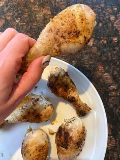 a person is holding a piece of chicken on a white plate with other food items