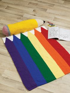 there is a crocheted rainbow rug on the floor next to an open book