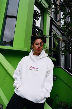 a woman standing in front of a green building Sporty Streetwear Hoodie With Screen Print, Sporty Hoodie With Screen Print For Streetwear, Trendy Hoodie With Logo Print For Streetwear, 90s Letter Print Hoodie For Streetwear, 90s Style Letter Print Hoodie For Streetwear, Throwback Hooded Hoodie With Logo Print, 90s Hooded Sweatshirt For Streetwear, 90s Style Hooded Sweatshirt For Streetwear, 90s Hooded Sweatshirt With Graphic Print