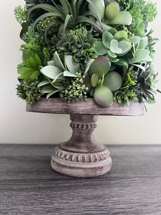 an arrangement of succulents and other greenery is displayed on a pedestal