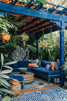 an outdoor living area with blue couches, potted plants and hanging lights on the ceiling