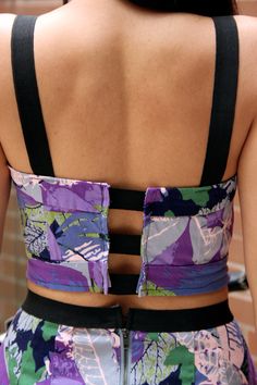 the back of a woman wearing a purple and green floral print sports bra with black straps