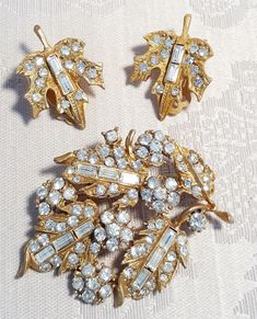 "This beautiful WEISS demi-parure consists of the brooch and matching clip earrings.  The brooch measures 1 5/8\" x 2 1/8\" wide. It has goldtone leaves and rosettes with inset clear rhinestone chatons and baguettes.  The matching clip earrings each measure 1\" x 3/4\" wide. They are also in excellent condition.  IMPORTANT: The pieces are signed \"TOP\" on the back which is made by Weiss for their \"top-of-the-line\" jewelry. The set is in excellent condition. A lovely vintage leaves and flowers demi parure to wear and add to your vintage jewelry collection. Please see our other vintage and antique jewelry listed. Always happy to combine shipping. Mark:   Pieces have been seen with both \"TOP\" and \"Weiss\" on them. This is Weiss's Top Of The Line Jewelry. Refer to this link for varificat Vintage Leaves, Gold Brooch, Gold Brooches, Enamel Flower, Clip Earrings, Vintage Costume Jewelry, Beautiful Gift Boxes, Clear Rhinestones, Vintage Costumes