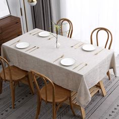 a dining room table is set with white plates and placemats, along with wooden chairs