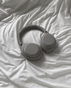 two headphones laying on top of a white sheet covered bed with sheets in the background