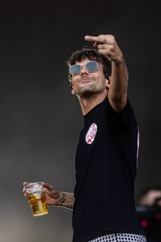 a man in black shirt and sunglasses holding up a glass with beer on the other side