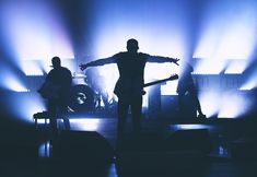 a man standing on stage with his arms outstretched in front of him and two other people behind him