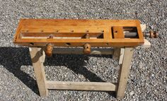 an old wooden bench sitting on top of gravel covered ground with wheels attached to it