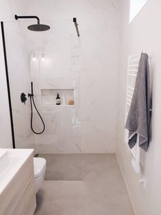 a bathroom with white walls and flooring has a black shower head on the wall