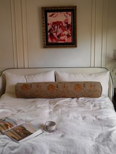 a bed with white linens and pillows in a bedroom next to a painting on the wall