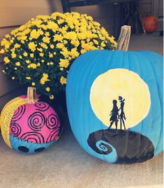 two painted pumpkins sitting next to each other on the ground with flowers in front of them