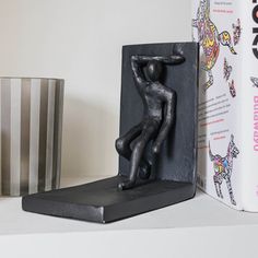 a black statue sitting on top of a white shelf next to a book and vase