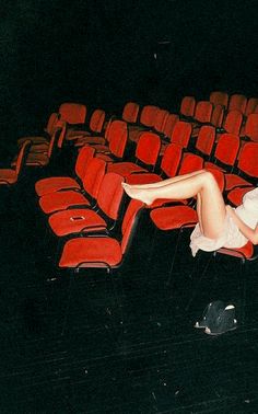 a woman laying on the floor in front of an empty theater auditorium with red seats