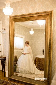 a woman is standing in front of a mirror wearing a wedding dress and looking at her reflection