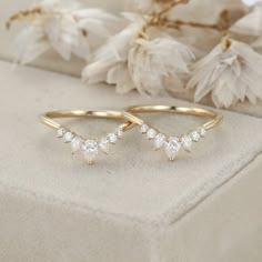 two gold rings with small white stones on them sitting next to some dried flower petals