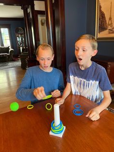 two boys sitting at a table playing with plastic rings and magnets on the table