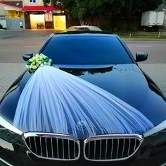 a black car with a white bouquet on it's hood is parked in front of a building