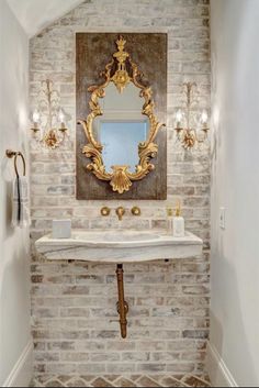 a bathroom with a sink, mirror and lights on the brick wall above it is decorated in gold