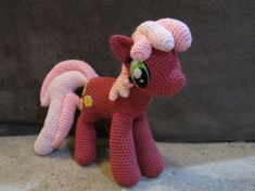 a crocheted pink pony sitting on top of a floor next to a gray wall