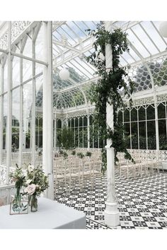 a white table topped with flowers and greenery next to a glass walled room filled with chairs