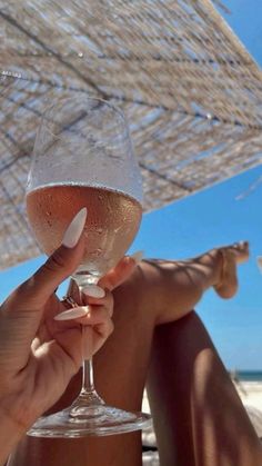 a person sitting on the beach holding up a wine glass with white wine in it