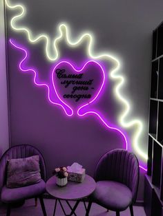 two purple chairs sitting next to a table in front of a wall with neon lights