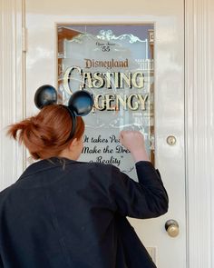 a woman with mouse ears on her head standing in front of a disney movie poster