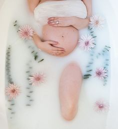 a pregnant woman laying in a bubble bath with flowers around her belly and breast on the side