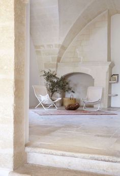 an indoor fireplace with two chairs and a potted plant