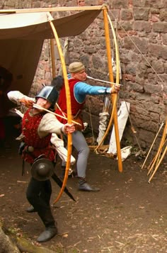 two men dressed in historical costumes are aiming arrows