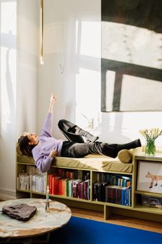 a woman laying on top of a couch next to a book shelf filled with books