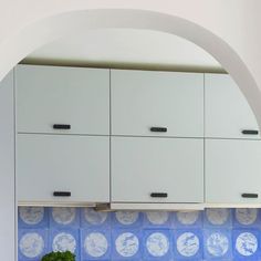 a kitchen with white cabinets and blue tiles on the backsplash, under an arched window