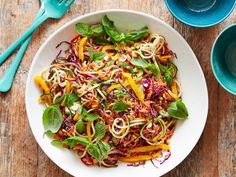 a white bowl filled with noodles and veggies on top of a wooden table