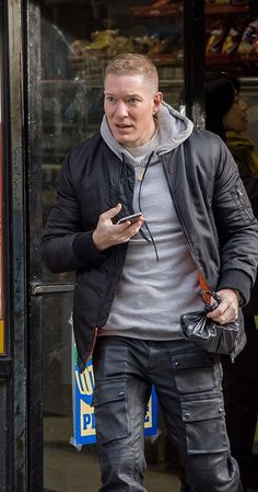 a man in grey shirt and black jacket looking at his cell phone while walking down the street