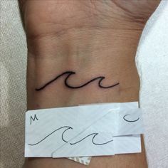 a wrist tattoo with waves on it and the letter m in cursive writing