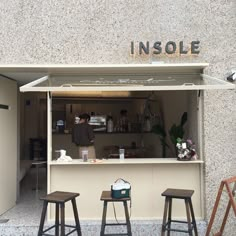 two stools sitting outside of a small bar with an insole sign above it