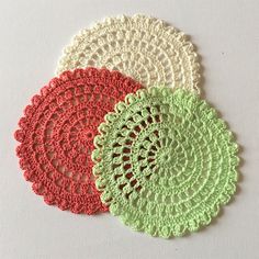 three crocheted doily on a white surface with red, green and beige colors