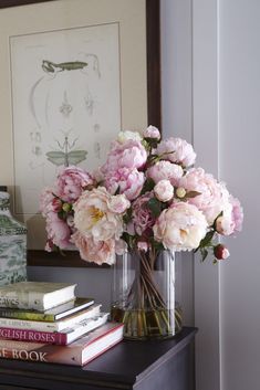 pink flowers in a vase sitting on top of a table next to books and a lamp