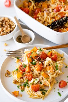 a white plate topped with pasta and veggies next to a bowl of nuts